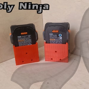 May include: Two 3D printed orange battery holders with black batteries inside. The holders have a textured surface and are designed to hold batteries upright. The text "3D Supply Ninja" is visible in the top left corner of the image.