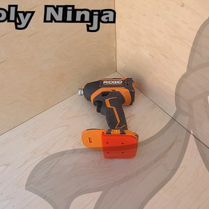 Pu&ograve; includere: Un trapano a batteria nero e arancione con un cacciavite a percussione rosso su una superficie di legno. Il trapano ha la scritta "RIDGID" stampata su di esso.