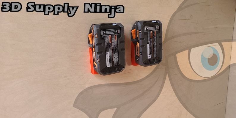 May include: Two black and orange battery chargers mounted on a light wood wall with a cartoon ninja painted on the wall. The text "3D Supply Ninja" is printed at the top of the wall.