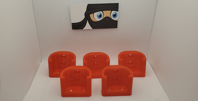 May include: Five bright orange 3D printed battery holders. The holders are designed to hold batteries upright and are ideal for organizing and storing batteries.