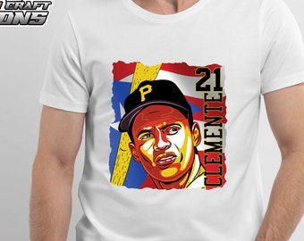 May include: White t-shirt with a colorful illustration of baseball player Roberto Clemente wearing a Pittsburgh Pirates cap and holding a bat. The illustration is set against a background of the Puerto Rican flag. The text "21 CLEMENTE" is printed on the right side of the illustration.