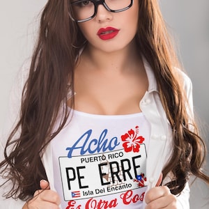 May include: White t-shirt with the words "Acho Puerto Rico" in blue script and a red hibiscus flower. The shirt also features a Puerto Rican license plate design with the words "PE ERRE" and "Isla Del Encanto".