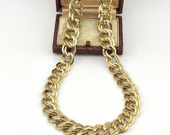May include: A gold-tone chain necklace featuring double interlocking oval links with a textured finish. The necklace is draped in a U-shape, with the top ends resting inside an open, rectangular, burgundy-colored jewelry box.