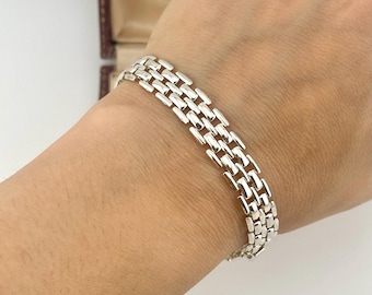 May include: A polished silver-tone bracelet featuring a multi-row link design with small, rectangular, interconnected segments. The bracelet has a smooth, reflective metallic finish and a flexible structure that wraps around the wrist area.