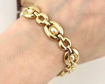 May include: A gold-toned bracelet with oval and rectangular links, each oval link featuring a small, round pearl. The bracelet is worn on a wrist, showcasing its polished finish and classic design. The bracelet is a timeless piece of jewelry.