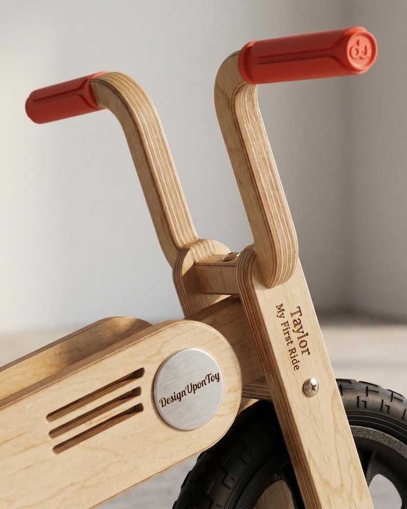 May include: A wooden balance bike with red handlebars. The bike features the text "Taylor My First Ride" and "Design Upon Toy". The bike has a silver emblem and black tires. The handlebars are approximately 10 inches wide.