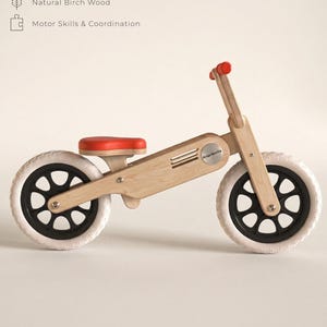 May include: A wooden balance bike with a red seat and handlebar grips. The bike has white tires and black wheels. The text "Bullberry Balance Bike" is at the top of the image. The bike is designed for children ages 2-5.