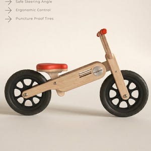 May include: A wooden balance bike with black tires and a red seat and handlebar grips. The bike has a natural wood finish and features the text "Bullberry Balance Bike".