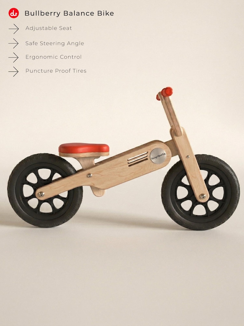 May include: A wooden balance bike with black tires and a red seat and handlebar grips. The bike has a natural wood finish and features the text "Bullberry Balance Bike".