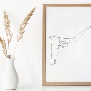 May include: A black and white line drawing of a longhorn cow's head with large horns, framed in a light wood frame.