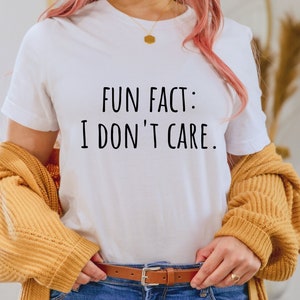 May include: White t-shirt with the text "FUN FACT: I DON'T CARE." printed in black.
