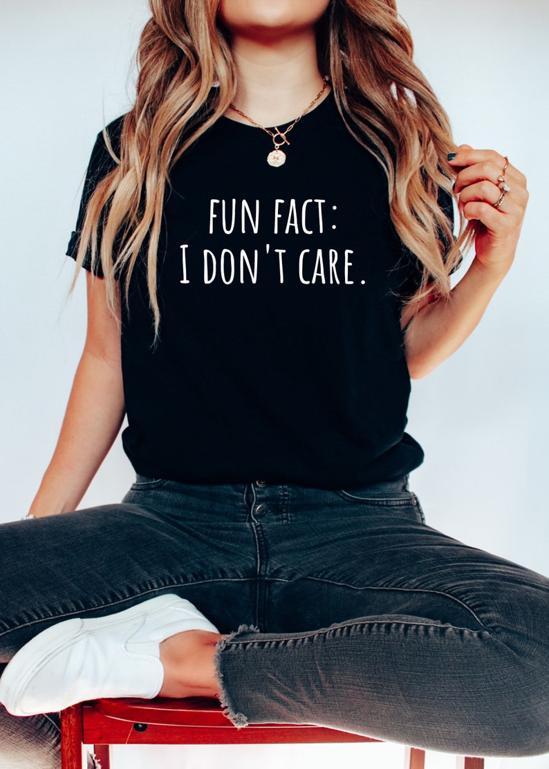 May include: A woman wearing a black t-shirt with the text "FUN FACT: I DON'T CARE." in white lettering. She is wearing black jeans and white sneakers.