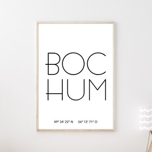 Könnte beinhalten: Ein Schwarzweißdruck mit dem Wort "BOCHUM" und den Koordinaten "49° 34' 22" N 56° 12° 71°0" auf weißem Hintergrund. Der Druck ist gerahmt und hängt an einer weißen Wand über einem Holztisch.