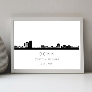 Könnte beinhalten: Schwarz-weiße Silhouette der Skyline von Bonn mit dem Städtenamen und den Koordinaten darunter. Die Skyline umfasst Gebäude, eine Kirche und eine Brücke.