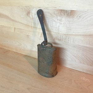 May include: A rusty metal cowbell with a long, curved handle. The bell is hanging from the handle and has a worn, aged appearance.