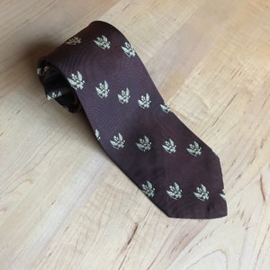 May include: A brown silk tie with a repeating pattern of green and gold stylized floral designs.