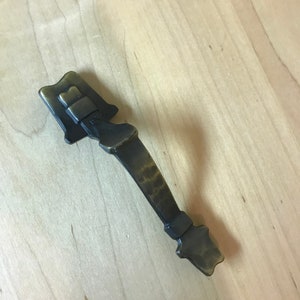 May include: A brass cabinet door pull with a unique, ornate design. The pull has a dark patina and a textured finish.