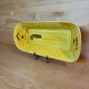 Puede incluir: Un plato de servir pan de cerámica amarillo con un diseño de cuchillo y las palabras "French Bread" a cada lado.