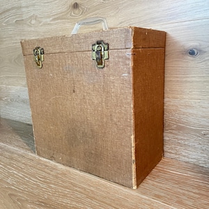 May include: A vintage wooden box with a clear plastic handle and metal clasps. The box is a light brown color and appears to be aged. The metal clasps are gold-toned. The box is rectangular and has a hinged lid.