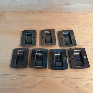 May include: Eight antique bronze door pulls with a rectangular shape and a black inset. The pulls have a slightly rounded edge.