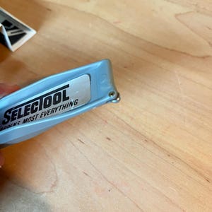 May include: A light blue SELECTOOL utility knife with the text "SELECTOOL SHARPENS MOST EVERYTHING" printed on a silver label. The knife is partially open, revealing the blade.