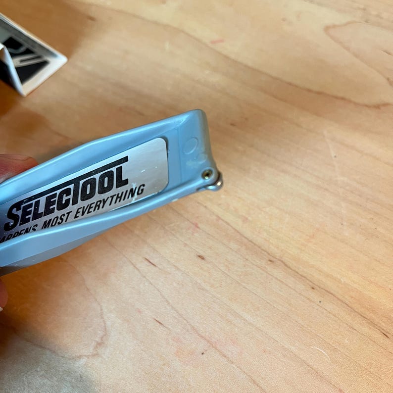 May include: A light blue SELECTOOL utility knife with the text "SELECTOOL SHARPENS MOST EVERYTHING" printed on a silver label. The knife is partially open, revealing the blade.