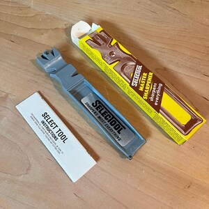 May include: A gray Select Tool knife sharpener with the text "SHARPENS MOST EVERYTHING". The packaging includes a yellow and brown box with "SELECTOOL MASTER SHARPENER" printed on it, and a white instruction sheet.