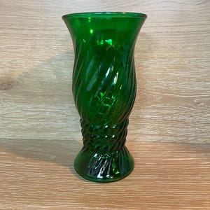 May include: A green glass vase with a twisted design. The vase has a flared top and a decorative rope-like detail near the base. The vase is approximately 8 inches tall.