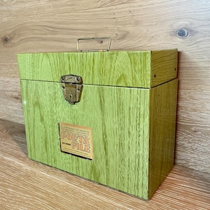 May include: A rectangular lime green metal storage box with a faux wood grain finish, a gold-colored metal handle, and a brass-toned latch. A rectangular label on the front reads: SAFE STORAGE FOR RECEIPTS TAX RECORDS DOCUMENTS PORTA FILE.