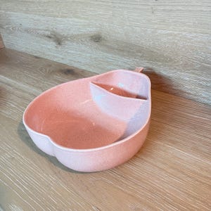 以下が含まれることがあります： 小さなコンパートメントが付いた、ピンク色の梨型のサービングディッシュ。お皿はまだら模様で、滑らかで光沢のある仕上がりです。このデザインは、どんなキッチンやダイニングにもユニークでスタイリッシュなアクセントになります。