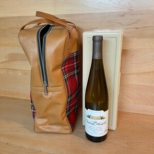 May include: A tan leather wine carrier with a red and black tartan accent, a bottle of Chateau Ste. Michelle Sweet Riesling wine, and a white wine case. The wine bottle has a white label.