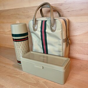 May include: A beige vintage travel set including a thermos, tote bag, and rectangular box. The thermos has a red and green stripe design. The tote bag has a vertical red and green stripe. The box is a solid beige colour.