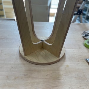 May include: The underside of a wooden stool with four legs that meet in the centre. The stool is made of light wood and has a circular base.