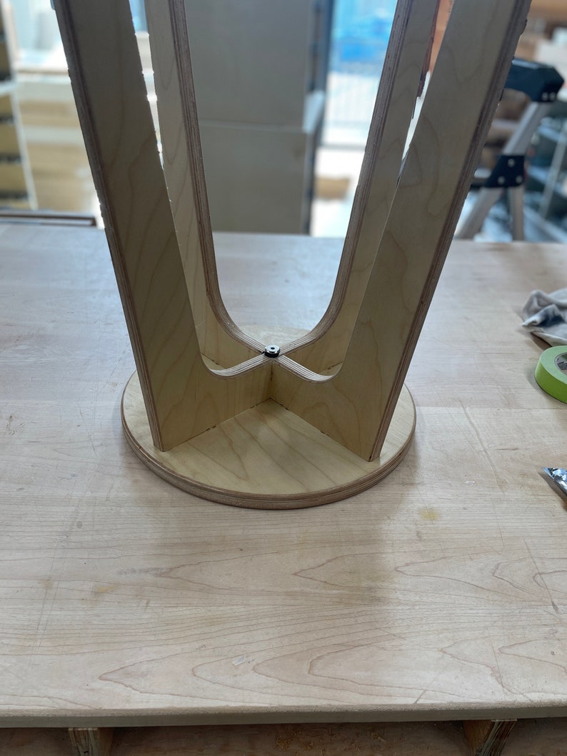 May include: The underside of a wooden stool with four legs that meet in the centre. The stool is made of light wood and has a circular base.