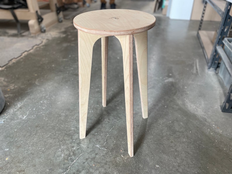 May include: A light wood stool with a round top and four legs. The stool is made of plywood and has a natural finish.