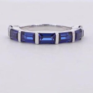 Peut inclure: Une bague en argent ornée de pierres précieuses rectangulaires bleu foncé. Les pierres sont disposées autour de l'anneau, créant un motif continu. L'anneau est présenté sur fond blanc.