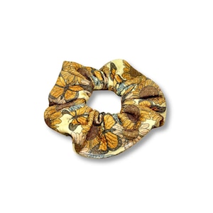May include: A scrunchie with a floral pattern in shades of yellow, brown, and orange. The fabric features a repeating design of flowers and butterflies. This hair accessory is a stylish addition to any hairstyle.