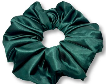 May include: A large, emerald green satin scrunchie. The hair accessory is circular with a gathered, pleated design. The fabric has a shiny, smooth texture. The scrunchie is set against a white background.