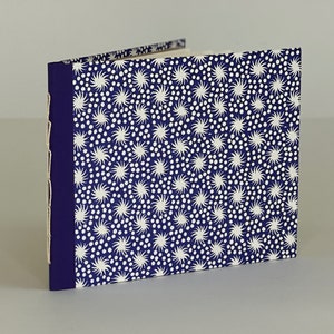 May include: A small, blue notebook with a white and blue patterned cover. The cover features a repeating pattern of white stars and dots.