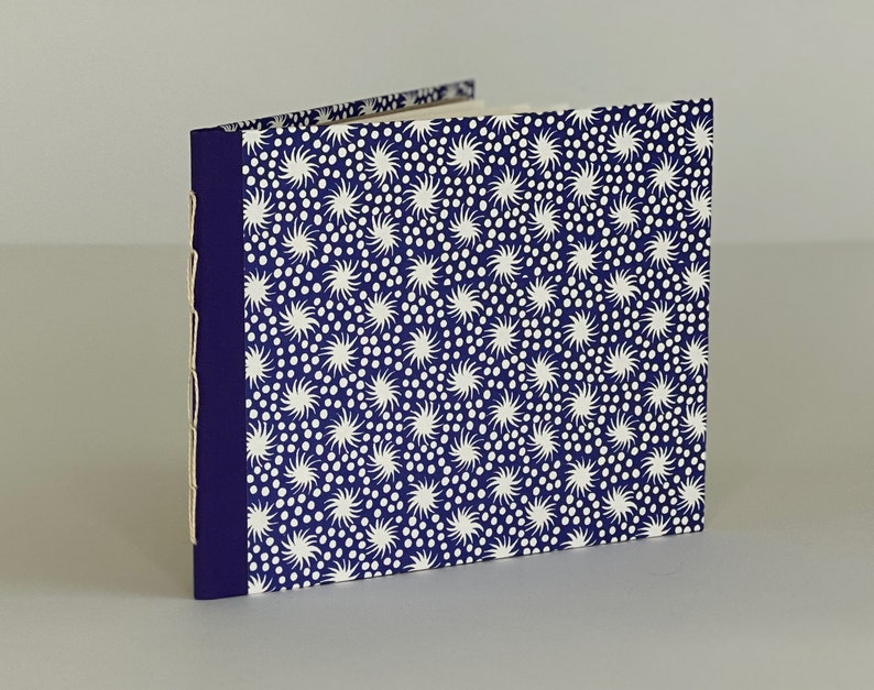 May include: A small, blue notebook with a white and blue patterned cover. The cover features a repeating pattern of white stars and dots.