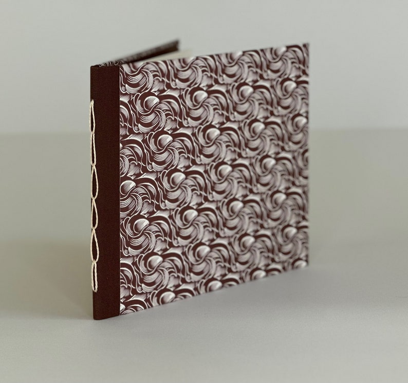 May include: A brown fabric-covered journal with a white swirling pattern. The journal has a white cord sewn along the spine.