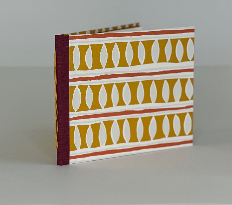 May include: A small, burgundy-colored book with a white and yellow patterned cover. The pattern features repeating white ovals on a yellow background with thin red lines.