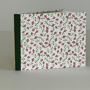May include: A small, white notebook with a red and green floral pattern on the cover. The notebook has a green spine and a yellow edge.