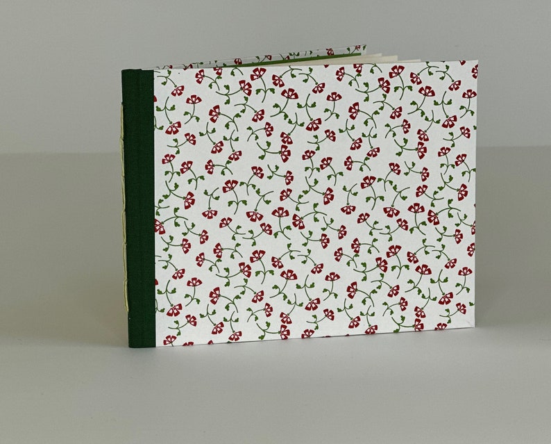May include: A small, white notebook with a red and green floral pattern on the cover. The notebook has a green spine and a yellow edge.