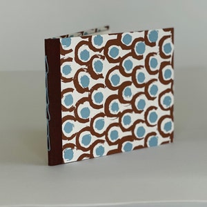 May include: A brown and white journal with a blue and brown abstract pattern on the cover. The journal has a brown spine and is closed.