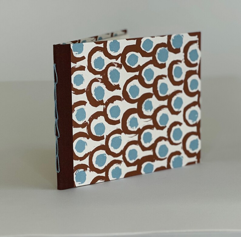May include: A brown and white journal with a blue and brown abstract pattern on the cover. The journal has a brown spine and is closed.