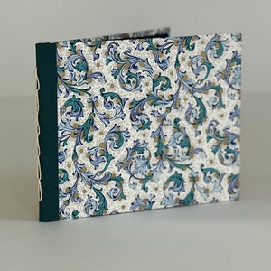 May include: A handmade journal with a green spine and white cover featuring a blue and gold floral pattern.