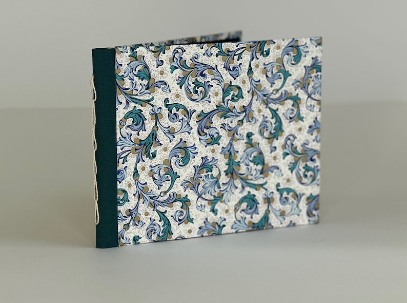 May include: A handmade journal with a green spine and white cover featuring a blue and gold floral pattern.