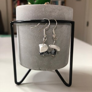 May include: A pair of silver dangle earrings with white and black stone accents. The earrings are hanging from a concrete planter.