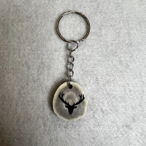 May include: A silver key chain with a round antler charm featuring a black silhouette of a deer head with antlers.